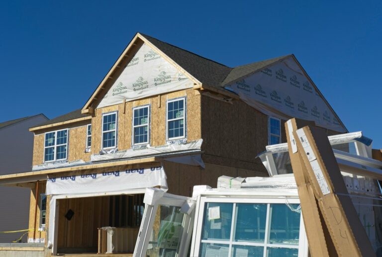 Homeowners review house plans beside a framed foundation with measuring tools and construction materials nearby.