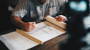 Homeowner reviewing residential construction plans beside a framed addition and permit documents.